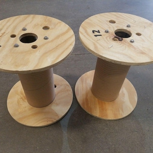 May include: Two wooden spools with a hole in the center and the number "12" written on the top. The spools are made of light brown wood and have a natural finish.