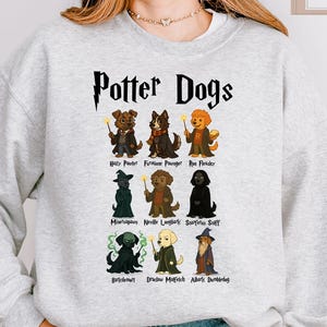 May include: A gray sweatshirt with the text "Potter Dogs" printed on the front. The text is in a black font and is surrounded by a lightning bolt. Below the text are nine illustrations of dogs dressed as characters from the Harry Potter series.