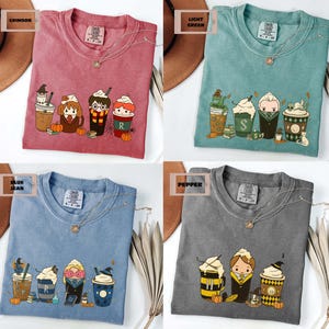 May include: Four t-shirts in crimson, light green, blue jean, and pepper colors. Each shirt features a graphic of cartoon characters in coffee cup designs, with pumpkins and books. The shirts have a crew neck and short sleeves.