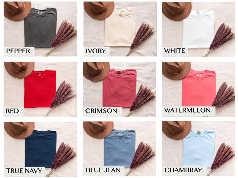 May include: A flat lay of ten different colored t-shirts with a hat on top of each shirt. The colors are pepper, ivory, white, red, crimson, watermelon, true navy, blue jean, and Chambray.