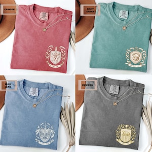 May include: Four t-shirts in crimson, light green, blue jean, and pepper colors. Each shirt has a crew neck, a small embroidered crest, and a gold necklace. The crests feature the words "Bravery", "Ambition", "Wisdom", and "Loyalty".