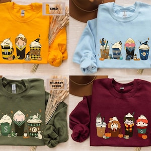 May include: Four crew neck sweatshirts in gold, light blue, military green, and maroon. Each has a cartoon design of themed coffee drinks and characters. The sweatshirts have long sleeves.