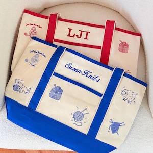 May include: Two canvas tote bags with red and blue trim. The top bag features red embroidery with the letters LJI and a gnome graphic. The bottom bag features blue embroidery with the text Susan Knits, a cat, a sheep, and yarn motifs.