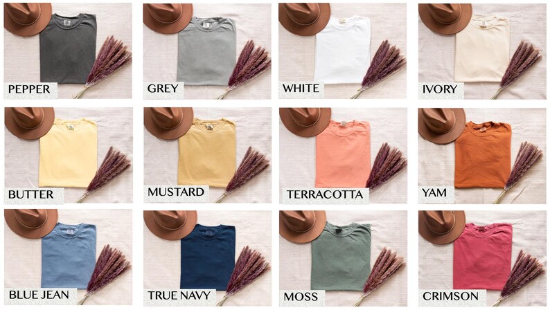 Op de afbeelding: Een verzameling van tien t-shirts in verschillende kleuren, waaronder peper, grijs, wit, ivoor, boter, mosterd, terracotta, yam, spijkerblauw, donkerblauw, mos en karmijnrood. De t-shirts liggen op een lichtbruine ondergrond met gedroogde bloemen.