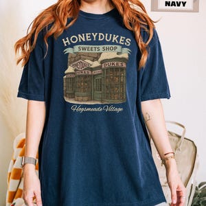 Op de afbeelding: Een marineblauw t-shirt met een afbeelding van Honeydukes Sweets Shop uit de Harry Potter-serie. De afbeelding bevat de tekst "Honeydukes Sweets Shop" en "Hogsmeade Village".