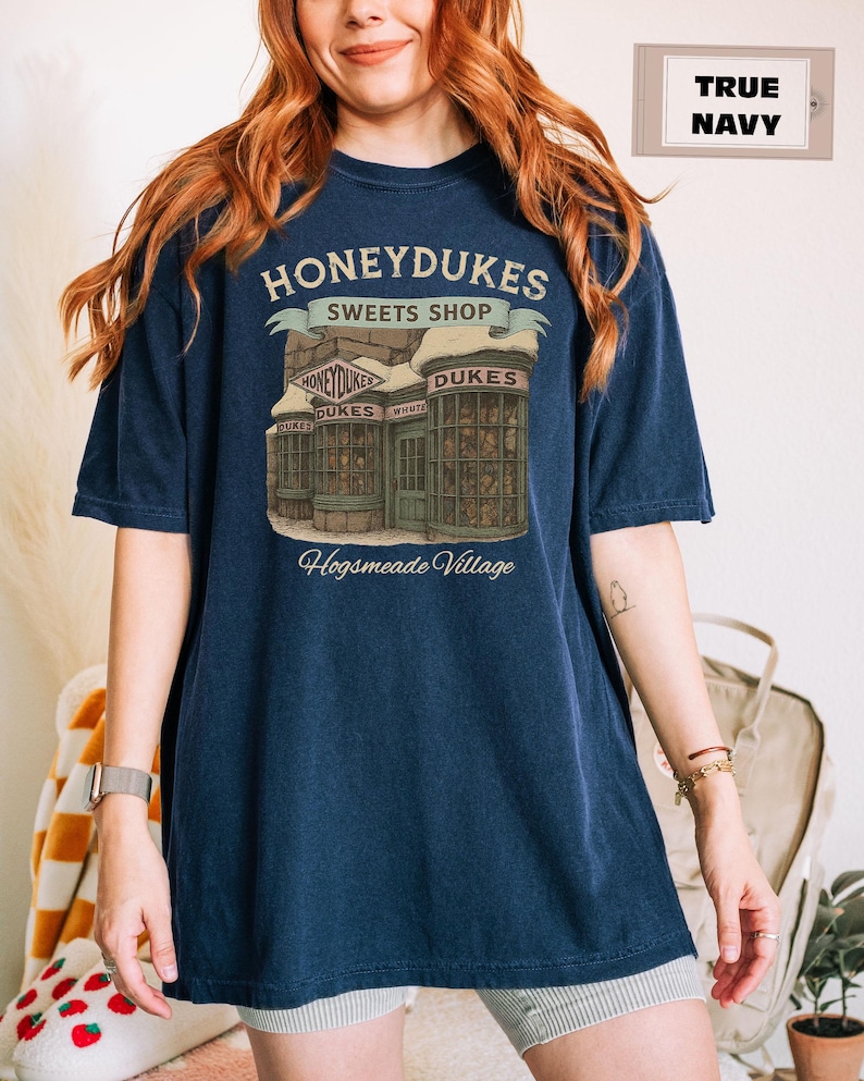 Op de afbeelding: Een marineblauw t-shirt met een afbeelding van Honeydukes Sweets Shop uit de Harry Potter-serie. De afbeelding bevat de tekst "Honeydukes Sweets Shop" en "Hogsmeade Village".