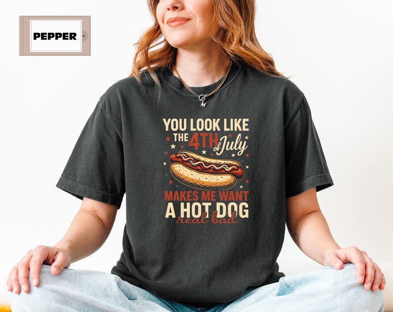 May include: A dark gray t-shirt with a graphic print of a hot dog and the text "You look like the 4th of July makes me want a hot dog real bad".