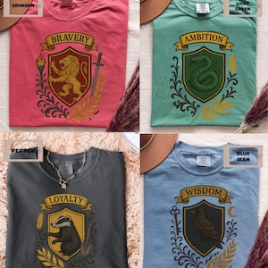 May include: Four t-shirts with different house crests from the Harry Potter universe. The crests are for Gryffindor, Slytherin, Hufflepuff, and Ravenclaw. The t-shirts are in the colors of each house: crimson, light green, pepper, and blue jean.