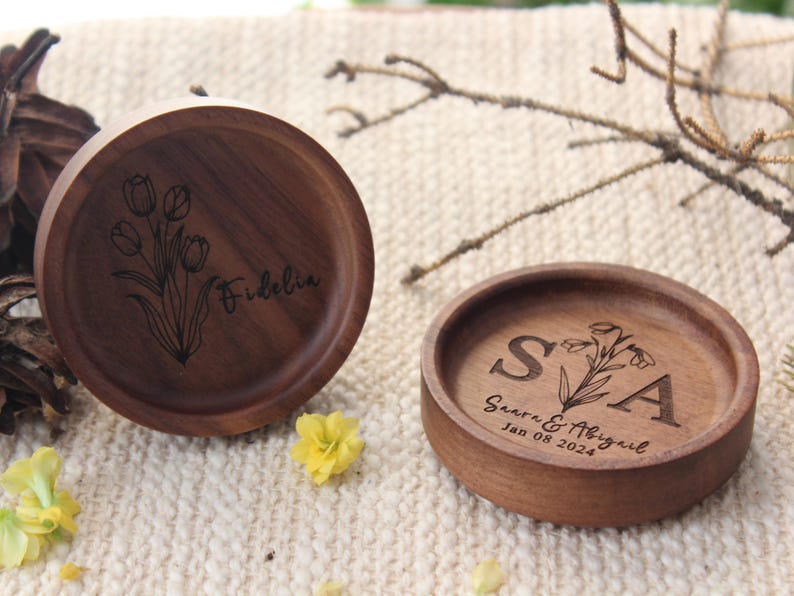 Puede incluir: Dos platos redondos de madera marr&oacute;n oscuro con dise&ntilde;os grabados. Uno presenta una ilustraci&oacute;n de tulipanes y el nombre Fidelia. El otro muestra las iniciales S y A, los nombres Saara & Abigail y la fecha 08 de enero de 2024.