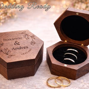 May include: Hexagonal wooden ring boxes, one closed and one open, displaying rings. The closed box is engraved with names and a date. The open box reveals rings set in a black velvet interior. Wedding Ready text is at the top.