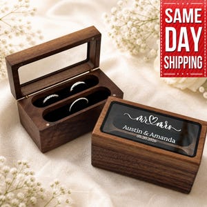 May include: Two wooden ring boxes, one open and one closed, with a clear top. The open box displays three rings in a black velvet interior. The closed box has a clear top with the text "mr & mrs" and a couple's names and wedding date.