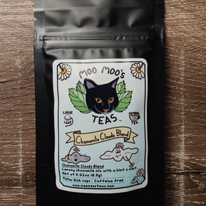 May include: Black tea bag with a label featuring a black cat, green leaves, and the text "Moo Moo's TEAS." The label reads "Chamomile Clouds Blend" and includes illustrations of clouds and daisies. The bag contains loose leaf herbal tea.