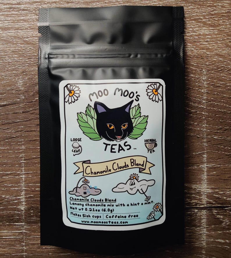 May include: Black tea bag with a label featuring a black cat, green leaves, and the text "Moo Moo's TEAS." The label reads "Chamomile Clouds Blend" and includes illustrations of clouds and daisies. The bag contains loose leaf herbal tea.