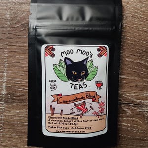 May include: A black tea bag with a label featuring a black cat, green leaves, and cinnamon sticks. The label reads "Moo Moo's Teas" and "Cinn-a-mintnado Blend." The net weight is 0.35oz (10.0g).