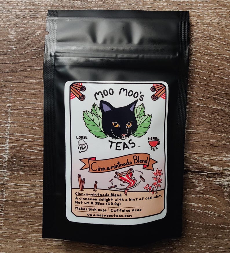 May include: A black tea bag with a label featuring a black cat, green leaves, and cinnamon sticks. The label reads "Moo Moo's Teas" and "Cinn-a-mintnado Blend." The net weight is 0.35oz (10.0g).