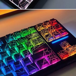 May include: A black mechanical keyboard with rainbow LED lights and keycaps featuring a spiderweb design.