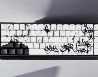 May include: A black and white keyboard with custom keycaps featuring a hand-drawn design of a person, flowers, and a butterfly. The keyboard has a black frame and white keys.