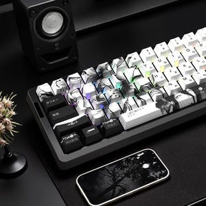 Peut inclure: Un clavier mécanique blanc avec des touches florales noires et blanches. Le clavier comporte des caractères japonais sur les touches. Le clavier est posé sur une surface noire avec un haut-parleur noir et un téléphone noir et blanc.