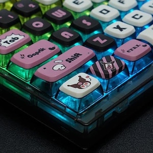 May include: A close-up of a keyboard with colorful keycaps. The keycaps feature various designs, including a skull, a heart, and a cartoon character. The keyboard is made of clear plastic and has a blue and green gradient.