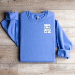 K&ouml;nnte beinhalten: Ein blaues Sweatshirt mit dem Text "WORK FROM HOME CLUB" in Wei&szlig; auf der Vorderseite.