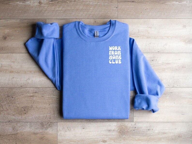 K&ouml;nnte beinhalten: Ein blaues Sweatshirt mit dem Text "WORK FROM HOME CLUB" in Wei&szlig; auf der Vorderseite.