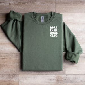 K&ouml;nnte beinhalten: Ein gr&uuml;ner Pullover mit dem Text "WORK FROM HOME CLUB" in Wei&szlig; auf der Vorderseite.