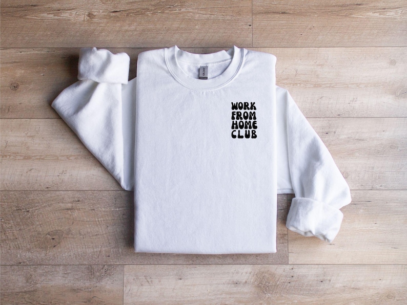 K&ouml;nnte beinhalten: Wei&szlig;er Rundhals-Pullover mit dem Aufdruck "WORK FROM HOME CLUB" auf der linken Brust.