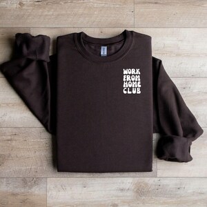 K&ouml;nnte beinhalten: Ein braunes Sweatshirt mit dem Text "WORK FROM HOME CLUB" in Wei&szlig; auf der Vorderseite.