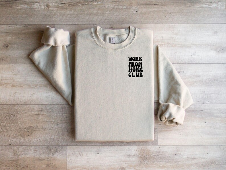 K&ouml;nnte beinhalten: Ein hellbeiger Pullover mit dem Aufdruck "WORK FROM HOME CLUB" in Schwarz auf der Vorderseite.
