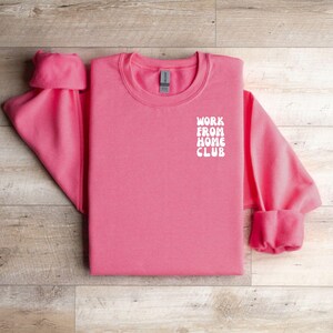K&ouml;nnte beinhalten: Rosafarbener Pullover mit dem Schriftzug "WORK FROM HOME CLUB" in Wei&szlig; auf der Vorderseite.