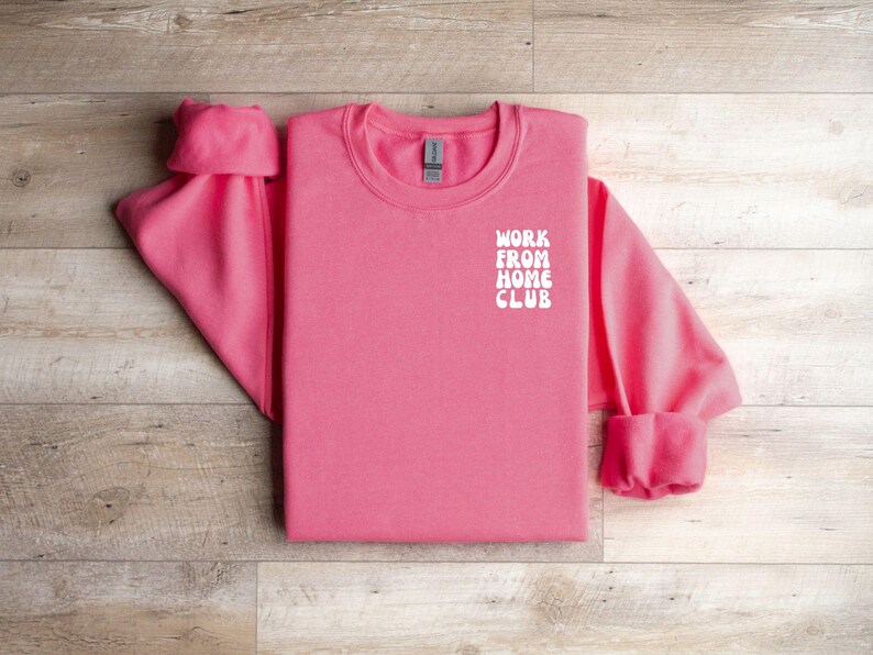 K&ouml;nnte beinhalten: Rosafarbener Pullover mit dem Schriftzug "WORK FROM HOME CLUB" in Wei&szlig; auf der Vorderseite.