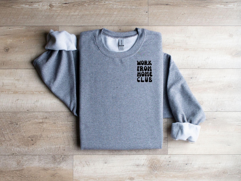 K&ouml;nnte beinhalten: Grauer Pullover mit dem Aufdruck "WORK FROM HOME CLUB" auf der Vorderseite.