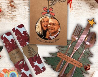 May include: A Christmas-themed arrangement featuring a greeting card with a photo, text, and a decorative ornament design. Includes red and white patterned napkins, cutlery, and a wooden Christmas tree.