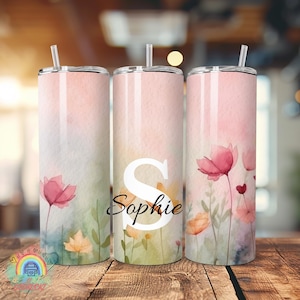 Könnte beinhalten: Drei Edelstahlbecher mit floralen Designs. Die Becher haben ein Aquarelldesign mit rosa Blumen, grünen Blättern und dem Namen "Sophie". Jeder Becher hat einen silbernen Deckel und Strohhalm.