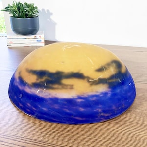 May include: A decorative glass bowl with a unique design. The bowl features a gradient of colors, with a yellow center transitioning to dark blue at the base. Dark cloud-like shapes are visible within the yellow area.