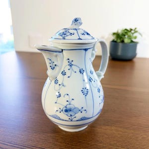 May include: A white porcelain creamer with a lid, decorated with blue floral patterns. The creamer features a spout, handle, and a small knob on the lid. The design is a classic, elegant style.