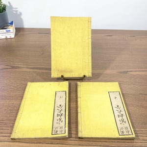 Peut inclure: Trois livres de couleur jaune avec du texte noir sur les couvertures. Le texte sur les couvertures est "木之国物語" et "上巻" et "下巻".