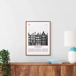 Könnte beinhalten: Schwarzweißfoto einer Reihe traditioneller Grachtenhäuser in Amsterdam, Niederlande. Das Bild ist in einem braunen Holzrahmen gerahmt und enthält den Text "AMS" und "AMSTERDAM".