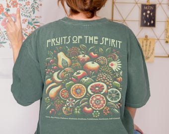 Może przedstawiać: Ciemnozielona koszulka z napisem "FRUITS OF THE SPIRIT" nad kolorową ilustracją różnych owoców. Koszulka zawiera również słowa "Love, Joy, Peace, Patience, Kindness, Goodness, Faithfulness, Gentleness, Self-Control."