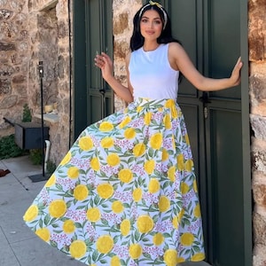 May include: A white sleeveless top paired with a long, flowing skirt. The skirt features a vibrant pattern of yellow lemons, green leaves, and small red accents on a white background. A yellow headband completes the outfit.