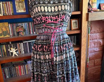 May include: A black and white patterned dress with pink and blue accents. The dress has a fitted bodice and a full skirt. It features a pink ribbon tie at the waist.