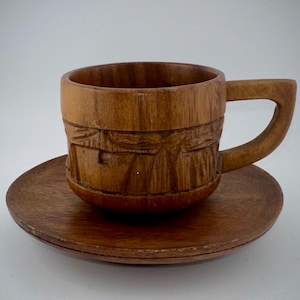 May include: A wooden coffee cup and saucer set. The cup and saucer are both carved with a decorative pattern. The cup has a handle.