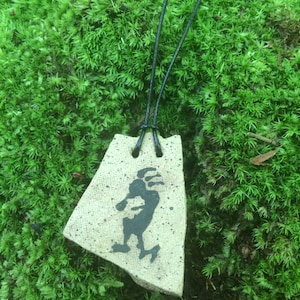 May include: A ceramic pendant necklace with a black and white silhouette of a person dancing. The pendant is attached to a black cord.