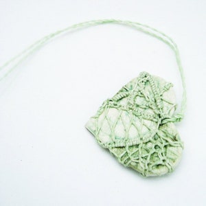 May include: A green heart-shaped pendant with a delicate crocheted design. The pendant is attached to a thin green string.