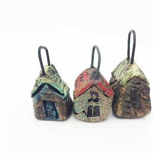 May include: Three small ceramic houses with different colored roofs and details. Each house has a black metal loop for hanging.