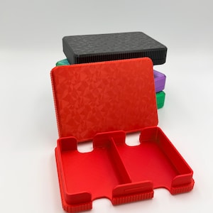 May include: A red, open, rectangular case with two compartments, featuring a textured geometric pattern on the lid. A stack of similar cases in black, green, and purple are visible in the background. The cases appear to be made of plastic.