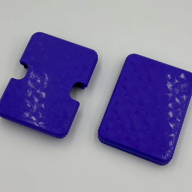 May include: Two vibrant purple card holders. One has a unique cutout design, while the other is a simple rectangular shape. Both have a textured, geometric pattern on the surface, adding visual interest to these functional accessories.