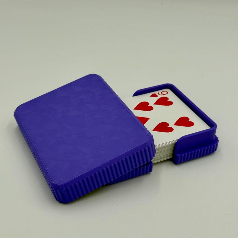 May include: A purple playing card case with a textured lid and a matching card holder. The case is open, revealing a deck of cards with red hearts and the number nine.