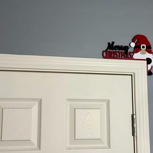 Medium shot of a white paneled door with the red and black gnome door corner decoration placed on the top right corner.