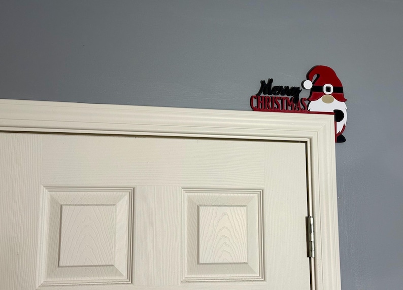 Medium shot of a white paneled door with the red and black gnome door corner decoration placed on the top right corner.